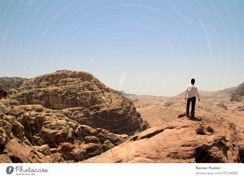 Junger Mann auf dem Gipfel eines Gipfels mit Blick über ein Tal in der rauen Landschaft von Petra, Jordanien Abenteuer Textfreiraum wüst die Welt erkunden