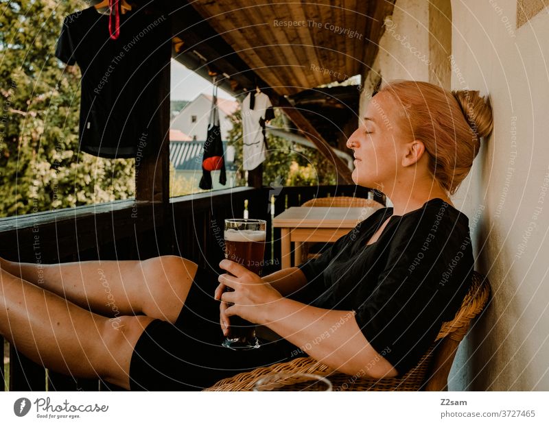 Junge Frau genießt ein Weissbier auf dem Balkon junge frau genuß trinken weißbier ausruhen entspannen träumen geschlossene augen sommer sonne wärme radfahren