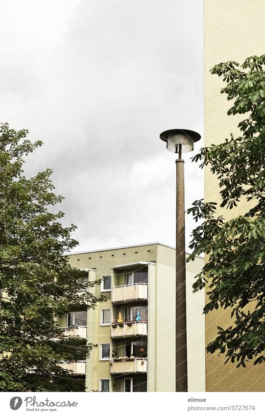 Urlaub auf Balkonien - Blick auf ein renoviertes modernes Mehrfamilienhaus mit individuell gestalteten Balkonen, vorbei an einer Straßenlampe, einer Hauswand und zwei Bäumen