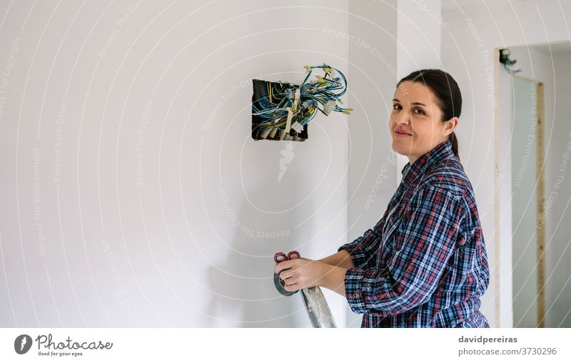 Elektriker, der an der Elektroinstallation eines Hauses arbeitet Elektrotechniker Frau Elektromonteur schauende Kamera Installation Lächeln verbindend