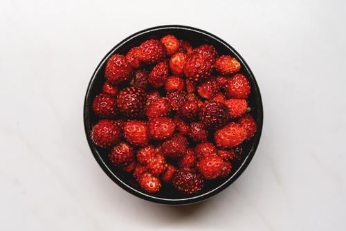 Draufsicht auf frische reife dunkelrote Walderdbeeren in einer schwarzen Schale auf weißem Hintergrund Erdbeeren Frucht Beeren süß Gesundheit Sommer Dessert