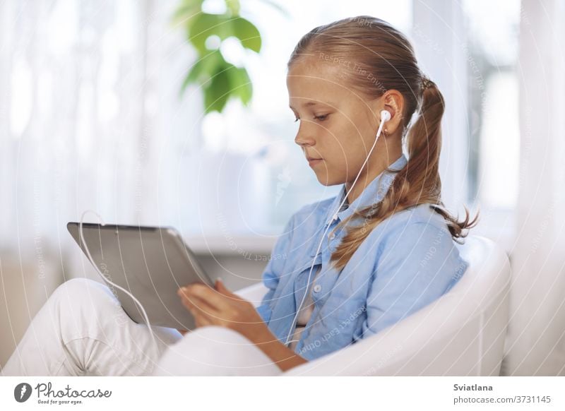 Ein Schulmädchen mit Kopfhörern sitzt auf einem Stuhl mit einem Tablett und macht während einer Online-Unterrichtsstunde ihre Hausaufgaben. Online-Unterricht, Online-Lernen. Soziale Distanz, Nahaufnahme