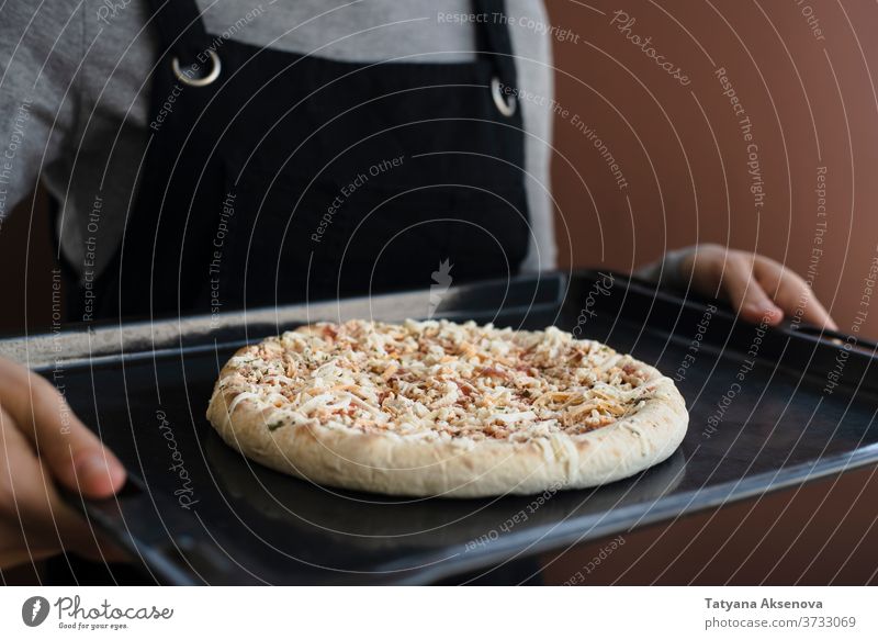 Frau hält Ofenblech mit Tiefkühlpizza in der Hand gefroren Pizza Lebensmittel ungekocht Komfortnahrung Fastfood Snack Kalorien schnell Käse Abendessen