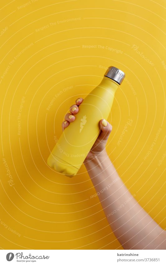 Nahaufnahme einer weiblichen Hand, die eine gelbe wiederverwendbare Stahlflasche auf gelbem Hintergrund hält Flasche Monochrom ökologisch Wasser Thermo hell