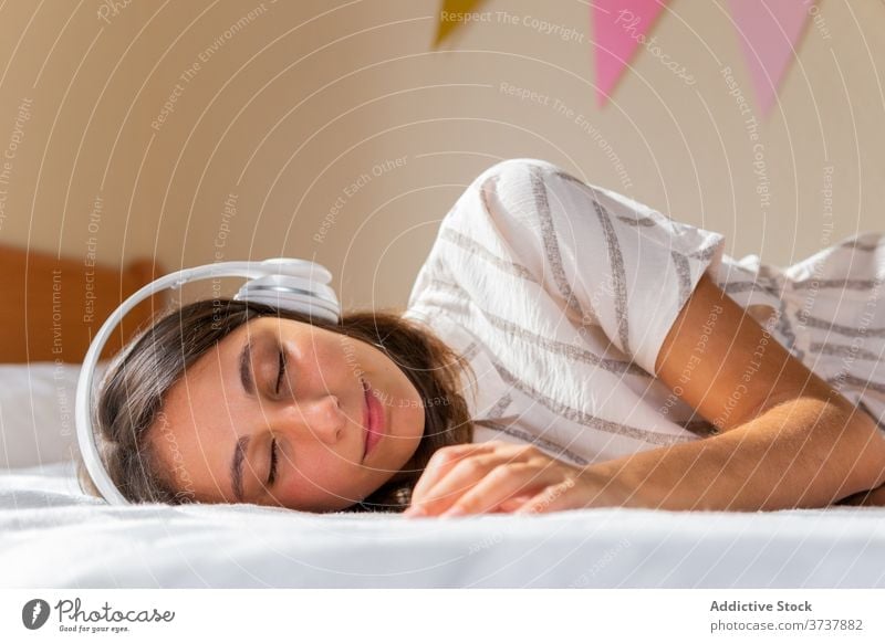 Junge Frau beim Musikhören auf dem Bett zuhören Kopfhörer heimwärts gemütlich Wochenende Augen geschlossen ruhen Lügen Apparatur Gerät Schlafzimmer jung