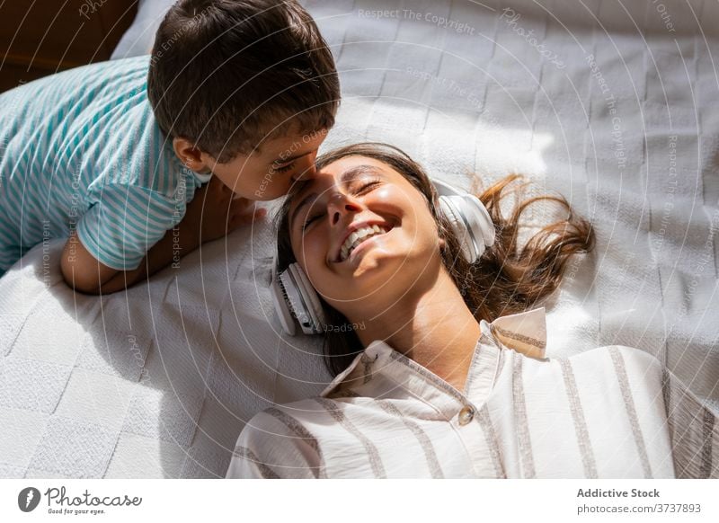 Junge küsst fröhliche Mutter in Kopfhörer Sohn Kuss zuhören Musik Glück Bett Wochenende ruhen Liebe Kleinkind Kind Frau Komfort unterhalten Schlafzimmer