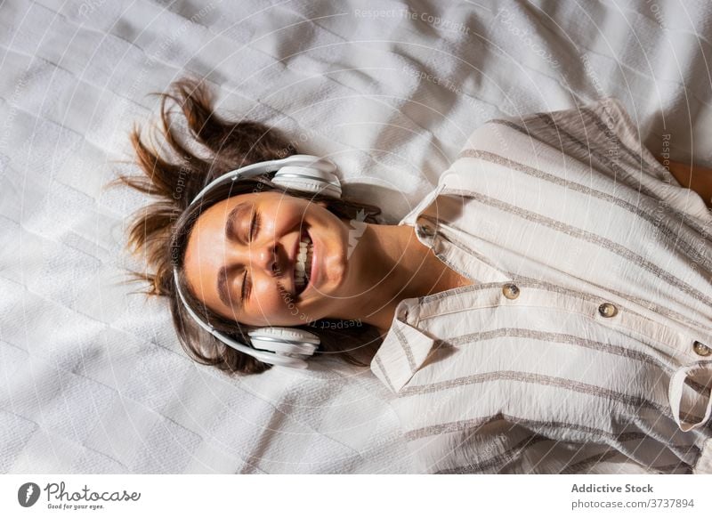 Zufriedene Frau mit Kopfhörern auf dem Bett Musik zuhören genießen Kind Zusammensein Drahtlos unterhalten Lügen Apparatur Glück Freude Schlafzimmer heiter