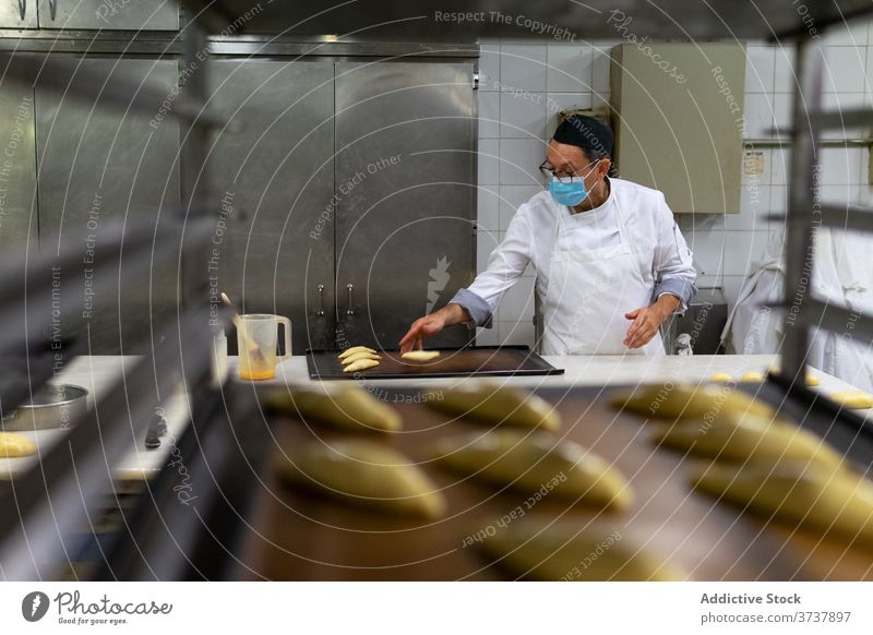 Ethnischer männlicher Koch in einer Bäckerei Mann Gebäck vorbereiten Uniform Küche medizinisch Mundschutz ethnisch Beruf kulinarisch Küchenchef Personal