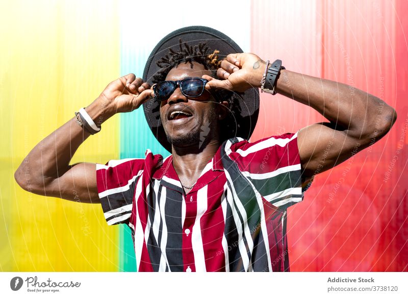 Stilvoller ethnischer Mann mit Sonnenbrille und Hut Mode trendy farbenfroh Streifen jung modern männlich Afroamerikaner schwarz Hipster mehrfarbig selbstbewusst