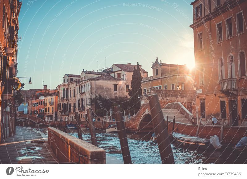 Noch ein Kanal in Venedig mit Booten und Brücken und diesmal auch mit der Sonne zwischen zwei Häusern romantisch Gegenlicht kitschig malerisch Abendlicht