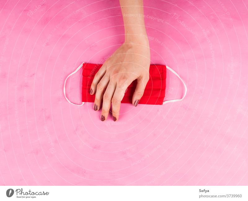 Rote Gesichtsmaske in Frauenhand auf rosa. Hahnrei-19 Mundschutz Hand Coronavirus COVID19 Gewebe handgemacht soziale Distanzierung Schutz Mode rot neue Normale