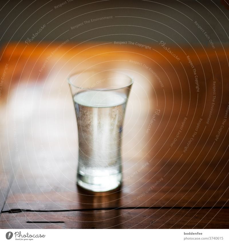 ein Wasserglas mit co2-Perlen am Glasinnenrand auf einem alten, braun lackierten Holztisch im morgendlichen Gegenlicht, leicht unscharf morgenlicht Morgen