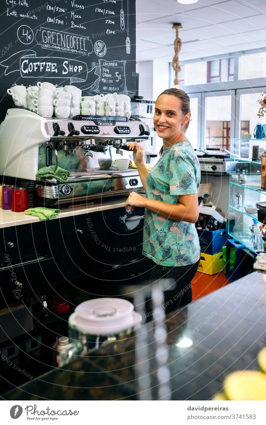 Weiblicher Barista bereitet Kaffeemaschine vor Frau Kaffeehaus vorbereitend Glück schauende Kamera Kellnerin Tasse Kantine trinken Herstellerin Café Werkstatt
