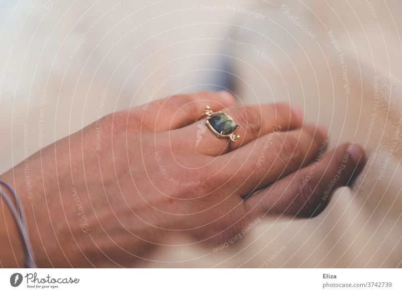 Eine Hand mit einem goldenen Ring mit grün schimmerndem Stein am Ringfinger Schmuck Frau Detailaufnahme Accessoire weiß Braut Ehering Hochzeit Verlobung