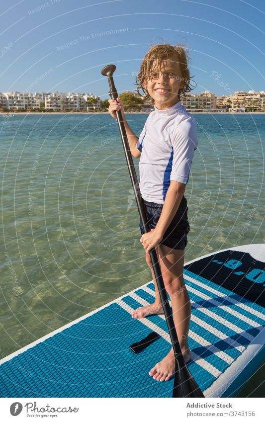 Porträt eines Jungen, der auf einem Paddel-Surfbrett steht, wobei das Paddel in Richtung der Kamera zeigt Lebensstile anstrengen Pose Surfen Stilrichtung stehen