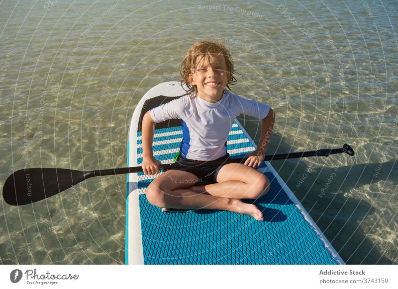 Blonde Junge sitzt auf einem Paddel Surfbrett mit einem Paddel im Meer schwimmen Lebensstile Pose Surfen müde bequem ruhig passen Erholung Freude Model