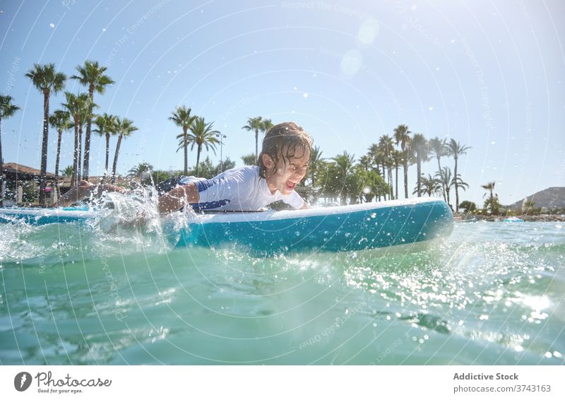 Junge liegend auf einem Surfbrett paddelnd mit den Händen Jugendzeit Vitalität Aufregung gestikulierend Wohlbefinden Geplätscher Stärke Surfen Teenager wellig