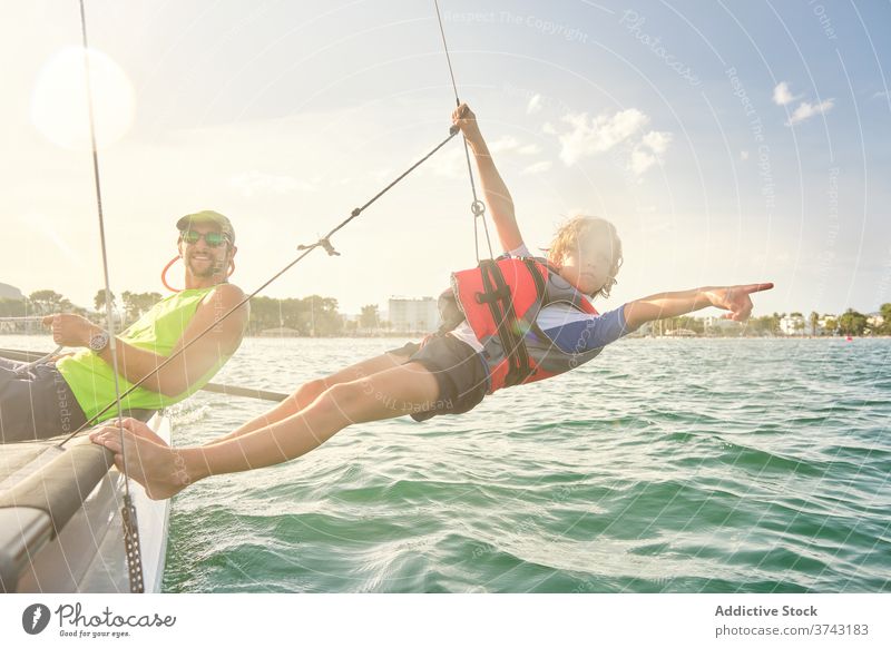 Junge, der an einem Seil von einem Boot aus auf das Meer hinaushängt und auf den Horizont zeigt Verantwortung Ausbilderin Rennen Lehrer Zeigen Unterstützung