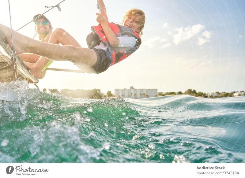 Junge mit Schwimmweste lacht, als er ein Seil von einem Boot packt, um Gegengewichte zu machen, die auf das Meer hinaushängen Verantwortung Lachen Ausbilderin