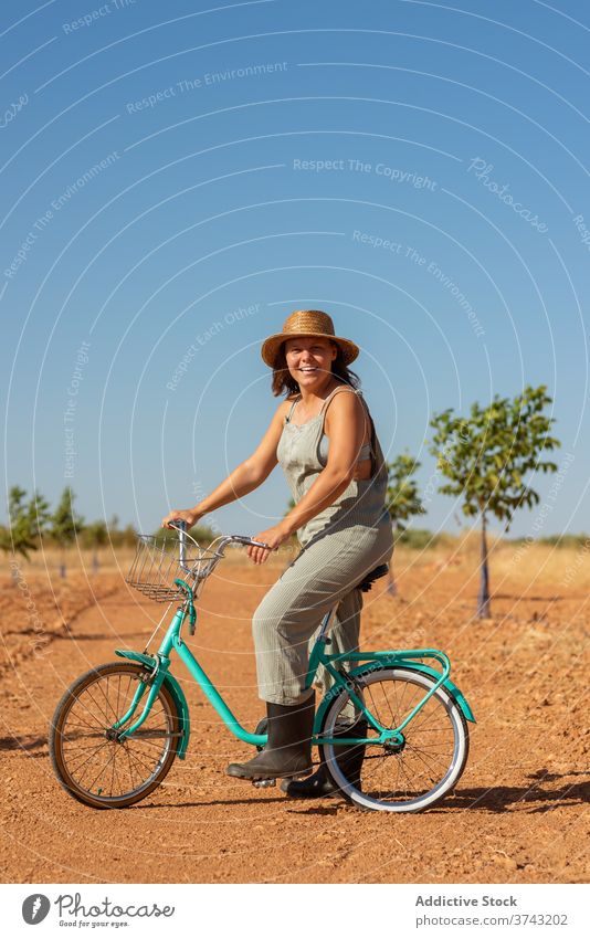Ruhige Frau auf dem Fahrrad in ländlicher Umgebung Straße Sand Sonnenlicht gesamt Landschaft Gelassenheit Sonnenbrille Jeansstoff Sommer Natur