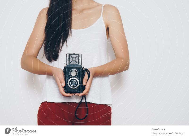 Frau, die eine Oldtimer-Kamera vor einem weißen Hintergrund hält Fotokamera altehrwürdig vereinzelt retro Fotografie Porträt schön Lifestyle Person attraktiv