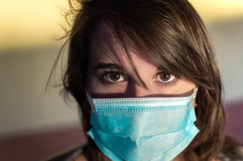 Nahaufnahme einer jungen Frau mit chirurgischer Maske und Blick in die Kamera. Person Mundschutz Korona starren Coronavirus Porträt Auge Gesicht tragend