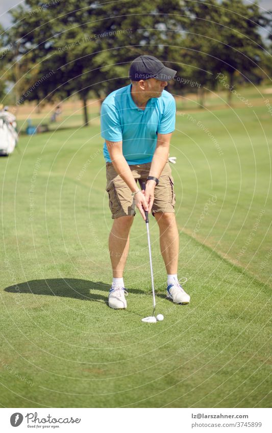 Golfer, der sich darauf vorbereitet, einen Schlag auf dem Fairway zu spielen, der sich mit dem Loch ausrichtet, bevor er seinen Schwung in einem sportlichen und aktiven Lebensstilkonzept ausführt