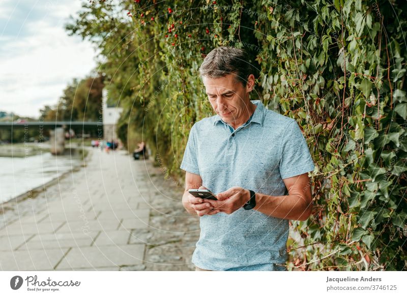 Mann schaut auf sein Handy und textet Telefon Mensch Erwachsener Lächeln Mobile Straße Technik & Technologie urban Nachricht Textfreiraum Außenaufnahme Freizeit
