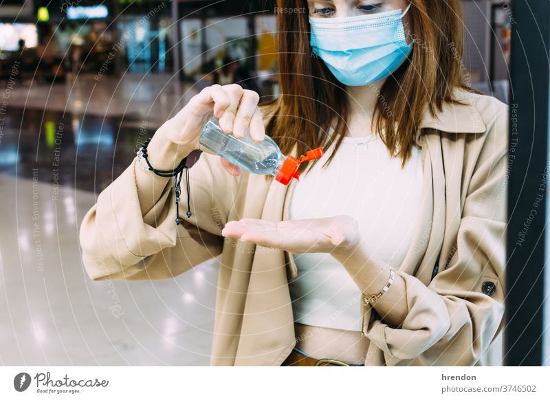 eine Frau, die eine Gesichtsmaske trägt und ihre Hände am Bahnhof mit hydro-alkoholischem Gel desinfiziert reisend Reise Virus Coronavirus Seuche Pandemie