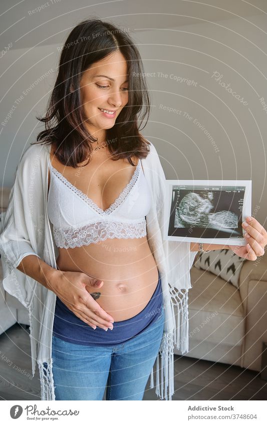 Glückliche schwangere Frau zeigt ein Ultraschallbild Scan Umarmen Magen Zärtlichkeit Mutterschaft Elternschaft Geburt heiter Bonden Lächeln Prüfung neugeboren