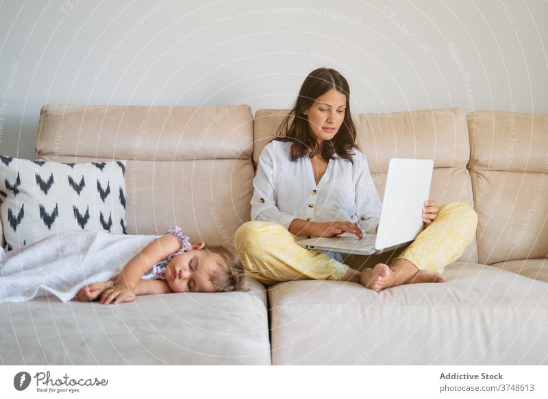 Frau arbeitet auf dem Sofa mit dem Laptop, während ein Kleinkind auf einer Seite schläft Ruhe Mutterschaft Verantwortung Zärtlichkeit träumend neugeboren