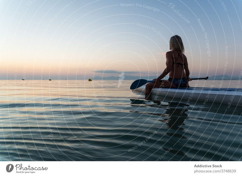 Anonyme Frau übt auf Paddleboard bei Sonnenuntergang Paddelbrett Surfer Zusatzplatine Reihe MEER Training Surfbrett Sommer Holzplatte sportlich sitzen