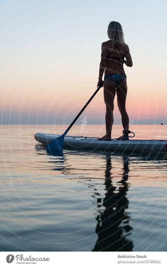 Anonyme Frau übt auf Paddleboard bei Sonnenuntergang Paddelbrett Surfer Zusatzplatine Silhouette Reihe MEER Training Surfbrett Sommer Holzplatte sportlich