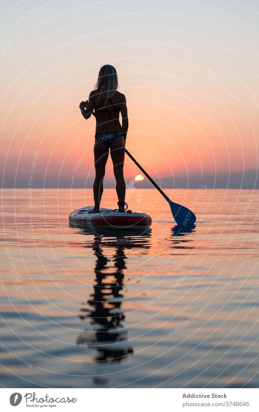 Anonyme Frau übt auf Paddleboard bei Sonnenuntergang Paddelbrett Surfer Zusatzplatine Silhouette Reihe MEER Training Surfbrett Sommer Holzplatte sportlich