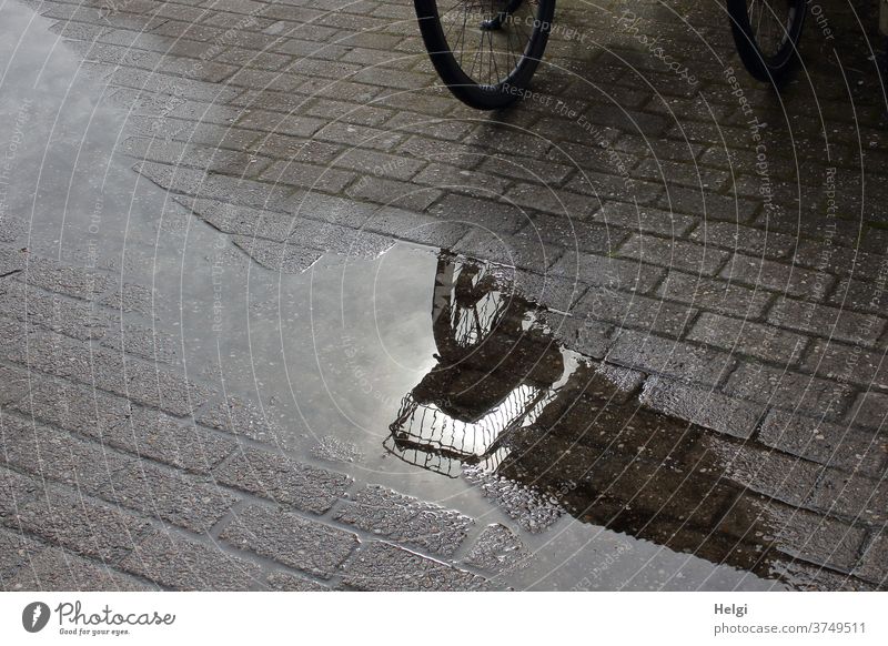 nach dem Regen - Detail eines Fahrrades mit Fahrradkorb auf Pflastersteinen spiegelt sich in einer Pfütze Spiegelung Detailaufnahme Licht Schatten Sonnenlicht
