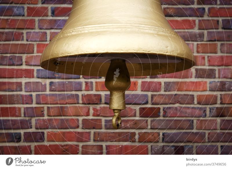 goldene Glocke mit Klöppel, im Anschnitt vor einer Backsteinwand Gold vergoldet Signal Schiffsglocke gegossen Nahaufnahme rot Glockenklöppel laut Töne Akustik