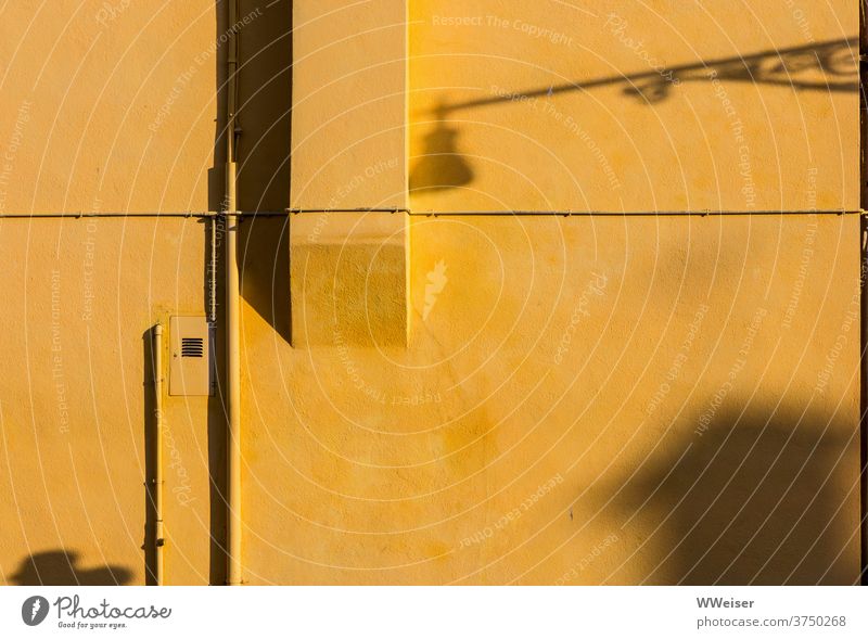 An einer gelben Hauswand treffen sich Abends verschiedene Schatten Wand Abendlicht Gebäude Laterne Vorsprung Straße Rohr Leitung Kabel geometrisch