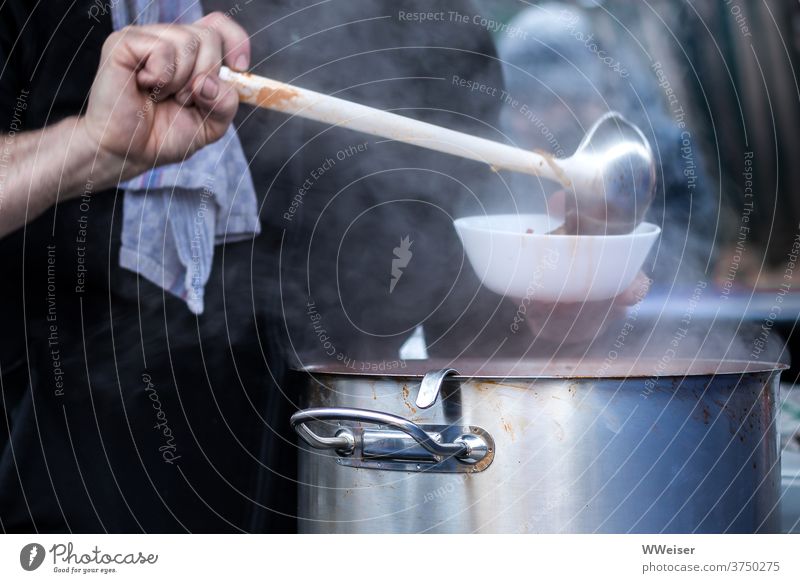 An einem kalten Tag wird leckere dampfende Suppe ausgeschenkt heiß Dampf Topf Kelle Schöpfkelle schöpfen Handtuch Ausschank ausschenken einschenken warm Hilfe