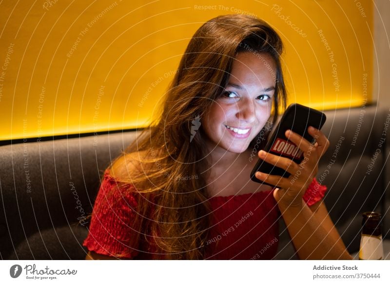 Lächelnde Frau mit Handy im Café warten Orden Smartphone benutzend gemütlich Atmosphäre dunkel Browsen Internet soziale Netzwerke online Gerät Apparatur Mobile