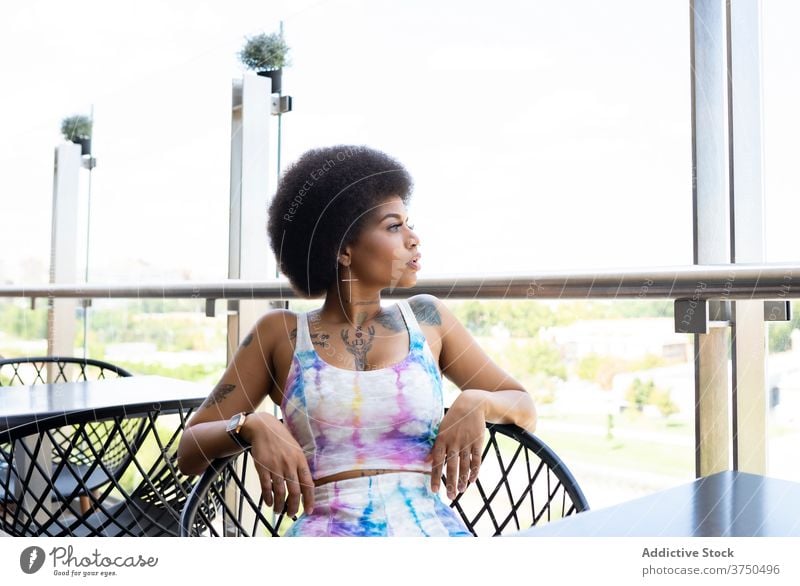Ruhige ethnische Frau auf der Sommerterrasse eines Cafés Terrasse warten Orden Windstille Afro-Look Frisur Großstadt schwarz Afroamerikaner Armsessel sitzen