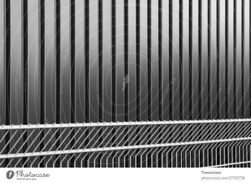 Kühle Fassade und ebensolcher Zaun Fassadenverkleidung Metall Linien Licht Schatten Außenaufnahme Gebäude Architektur Absperrung Schwarzweißfoto nüchtern