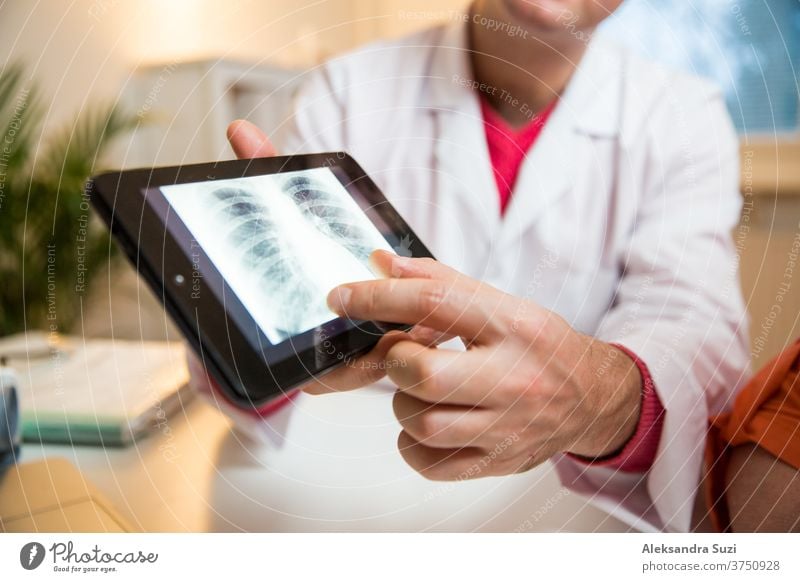 Lächelnder männlicher Arzt hält digitale Tablette in der Hand und zeigt dem Patienten im Krankenhaus die Testergebnisse. Röntgenbilder auf dem Bildschirm. Kranke ältere Frau, die einen Arzttermin hat. Ärztliche Beratung.