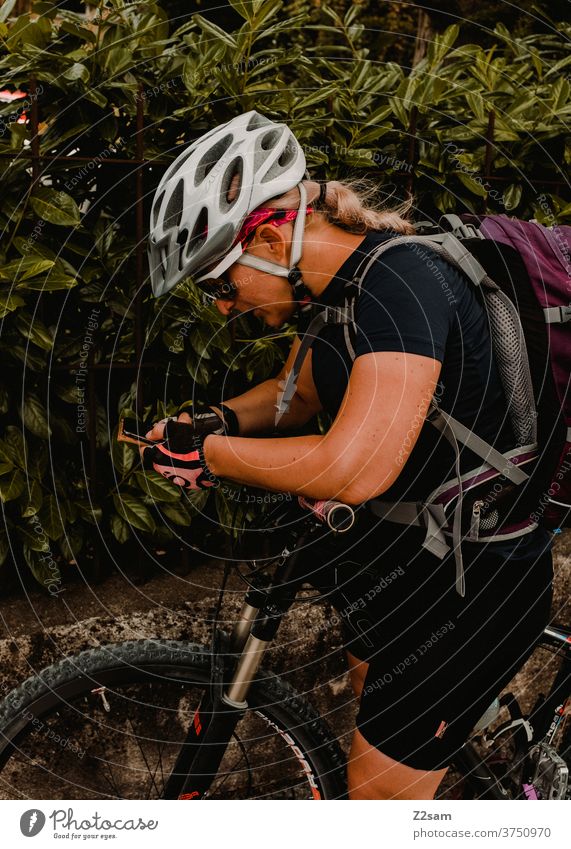 Radfahrerin auf einer Radtour sucht den Weg auf ihrem Smartphone Mountainbike Natur Landschaft Bayern Schutzhelm Sonnenbrille Sportbekleidung Trikot ruhen Pause