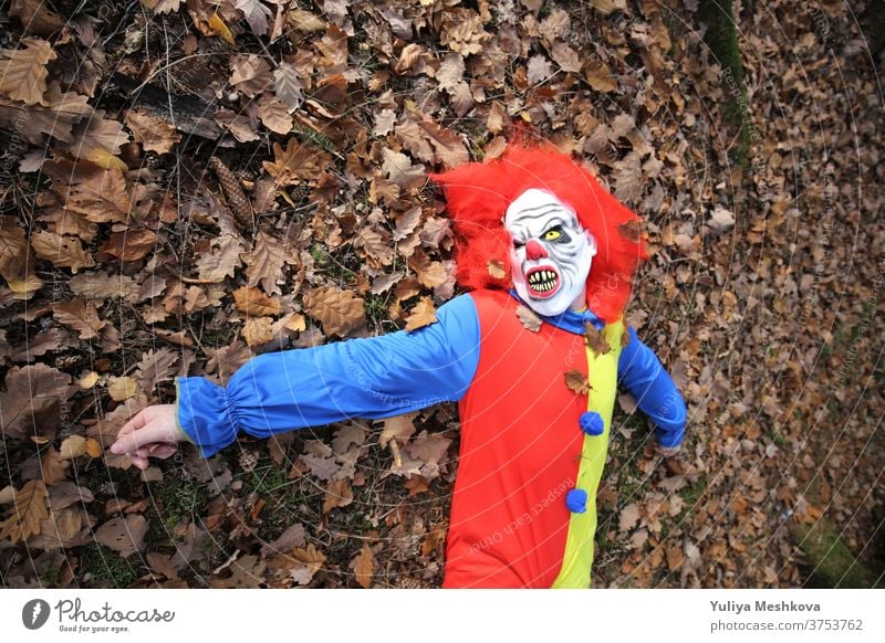 Halloween Party. Gruseliger Clown mit roten Haaren liegt im Herbstlaub gruselig Kostüm Clown Overalls Wald Feiertage Oktober Festival Karneval Konzept Horror
