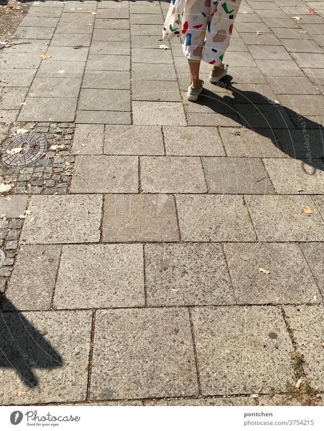 Beine einer Frau in einer weißen culotte mit bunten geometrischen Formen auf einem gepflasterten Gehweg. Schattenwurf. Gehen, Fußgänger Mode kleidung fußgänger