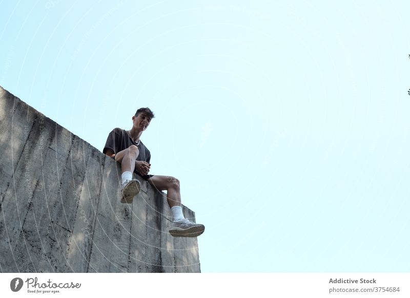 Junger Mann sitzt auf Stein Grenze in der Stadt Wand Großstadt sich[Akk] entspannen Le Parkour Gebäude Beton hoch Fähigkeit männlich ruhen Training Lächeln jung
