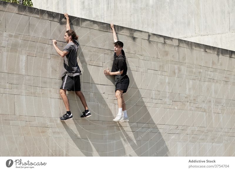 Starke Männer hängen an der Wand eines Gebäudes Le Parkour Freestyle Risiko Stunt urban Zusammensein extrem Trick Großstadt Gefahr Mut jung aktiv gutaussehend