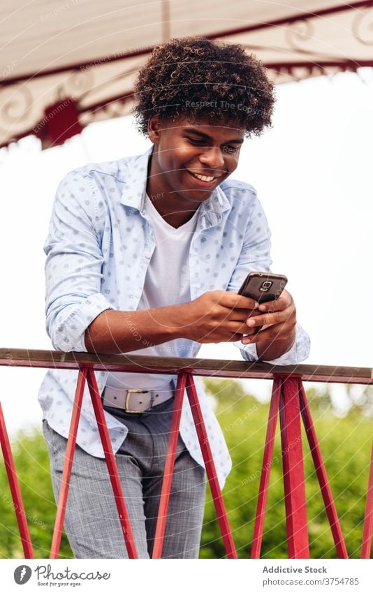 Glücklicher schwarzer Mann in der Stadt stehend Großstadt beobachten Sommer Straße Metall Reling Browsen zuschauend Smartphone männlich Telefon ethnisch