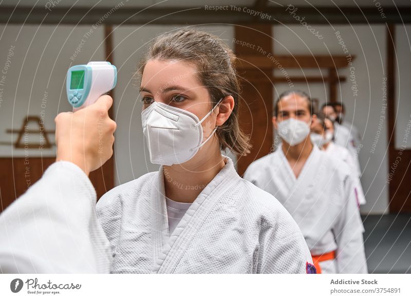 Menschen mit Masken und einem Kimono, die den Covid-Temperaturtest in einer Turnhalle durchführen Scan Schüler Seminar Personal Trainerin Fieber lernen Pandemie