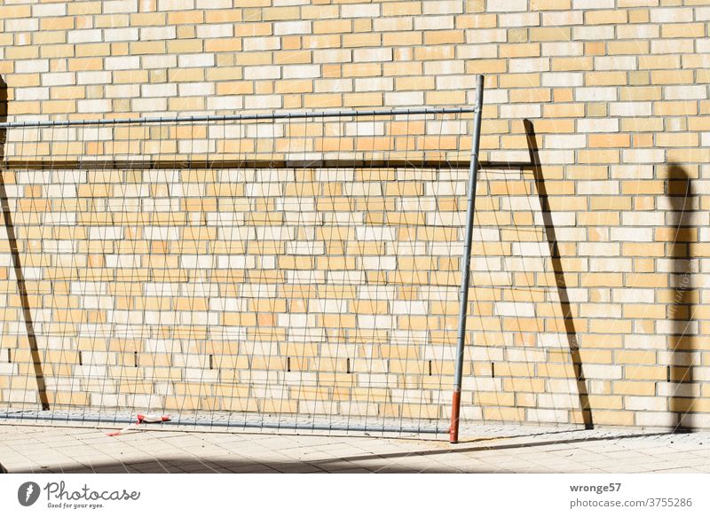 Ein Feld eines Bauzauns lehnt an einer Wand aus Klinkersteinen und zeichnet einen Schatten darauf Zaun Baustelle Zaunfeld Sicherheit Absperrung Außenaufnahme